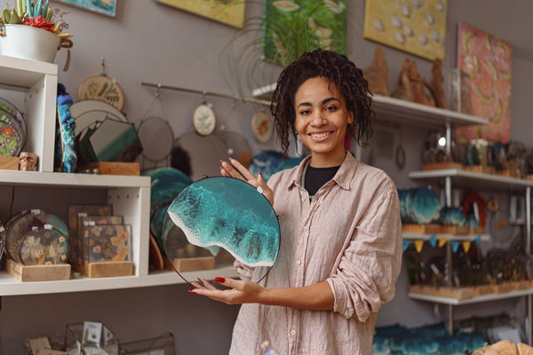 A woman holding a finish epoxy resin piece with pigmented epoxy "waves" representing ocean water.