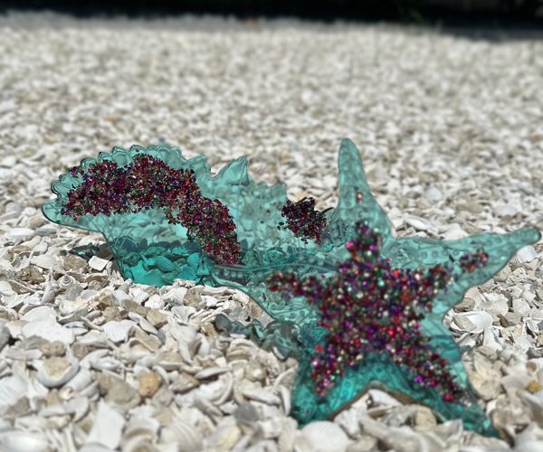 Two epoxy resin art pieces, one shaped like a starfish and another shaped like a seashell. Both were colored with Pigmently's Teal, Neon Green, and Peacock Blue epoxy resin dyes.
