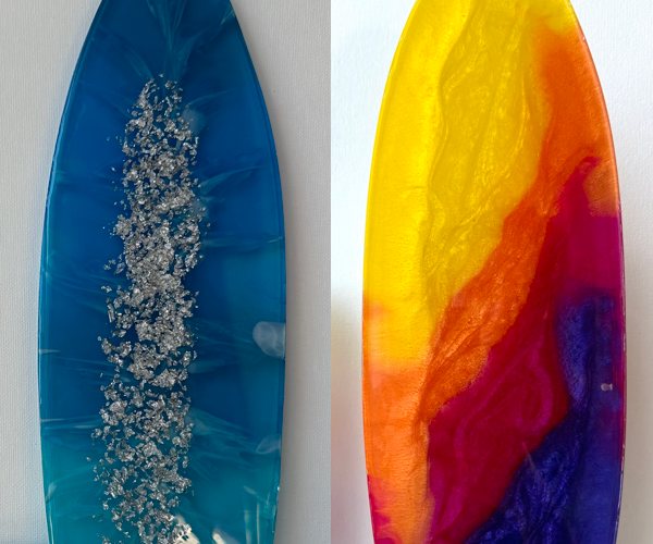 Two surfboard-shaped resin pieces, one made with liquid dyes and the other made with powder pigments.