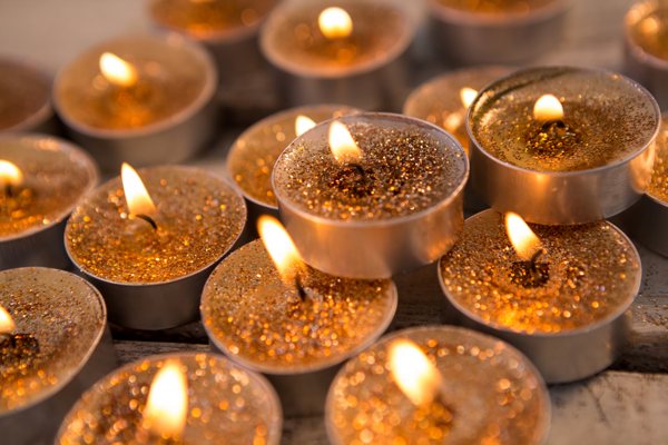 A large number of lit candles with a sprinkling of gold powder on top.