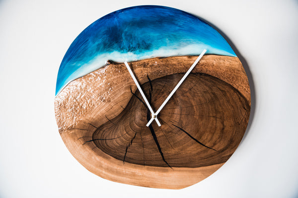 A resin art piece of a clock with a beach-themed background made using wood and blue and white epoxy pigments.