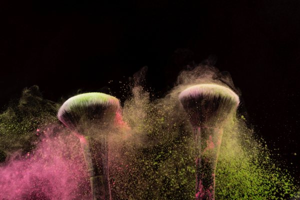 Two wide makeup brushes dispersing different colored mica powders.